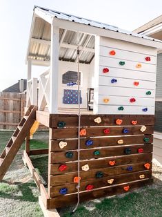 an outdoor play structure made out of pallet wood and painted white with colorful rocks on the side