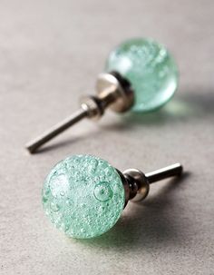 two green glass knobs with metal posts on top of a gray surface and one has a smiley face drawn on it