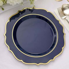 a blue plate with gold trim sits on a white table cloth next to silverware