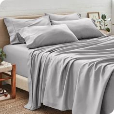 a bed covered in grey sheets and pillows