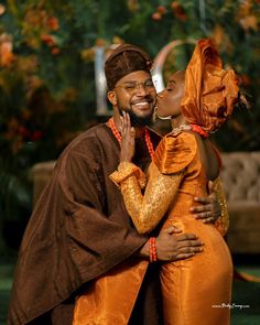 a man and woman dressed in african clothing kissing on the cheek while standing next to each other