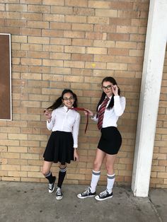 two girls dressed in school uniforms standing next to a brick wall and posing for the camera