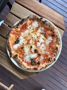 a pizza sitting on top of a white plate next to a wooden table covered in cheese