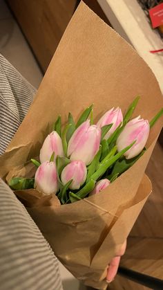 a bouquet of pink tulips in a brown paper wrapper on someone's lap