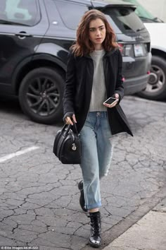 a woman is walking down the street with her hand in her pocket and looking at her cell phone