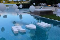 an outdoor pool with white balloons floating in the air next to chairs and tables set up around it