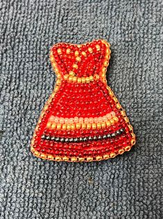 a red and yellow beaded brooch sitting on top of a gray cloth covered surface