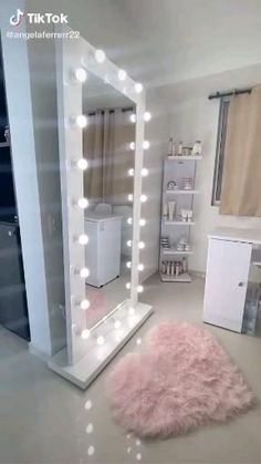 a large mirror with lights on top of it in a room next to a pink rug