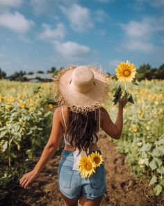 a woman walking through a field with sunflowers in her hand and a straw hat on her head