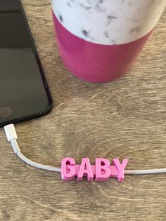 the word gaby spelled with pink letters next to a cell phone on a table