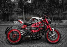 a red and black motorcycle parked on top of a brick road in front of trees