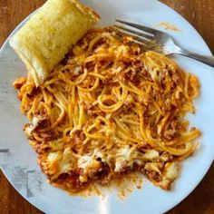 a white plate topped with pasta and meat next to a burrito on top of a wooden table