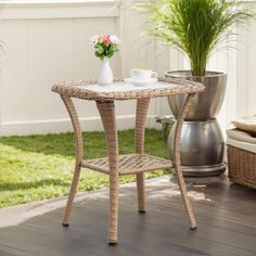 a wicker table with two cups on it in front of a potted plant