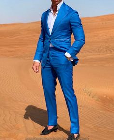 a man in a blue suit standing in the sand with his hands in his pockets