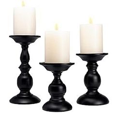 three black candle holders with white candles in them