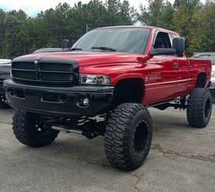 a red truck parked in a parking lot next to other cars and trucks with large tires