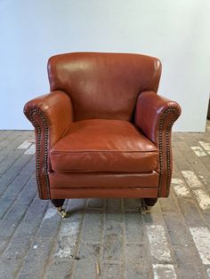 a brown leather chair sitting on top of a brick floor next to a white wall