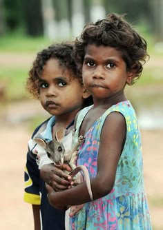 two young children holding a small animal in their hands and looking at the camera with an intense look on their face