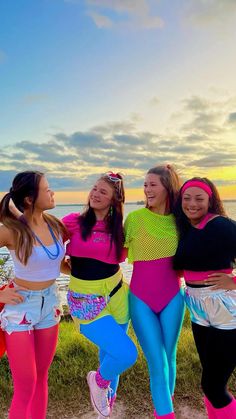 four girls are posing for the camera with their arms around each other and one girl is wearing bright colored clothing