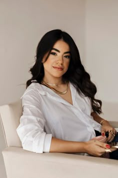 a woman sitting in a white chair with her hands on her lap and looking at the camera