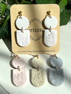 four pairs of earrings sitting on top of a white table next to green leafy plants