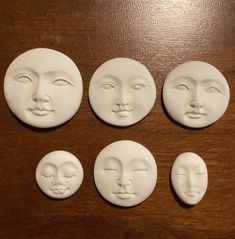 four faces are shown in white clay on a wooden surface, each with different shapes and sizes