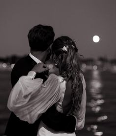 a man and woman standing next to each other in front of the ocean at night