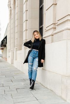 a woman leaning against a wall wearing ripped jeans