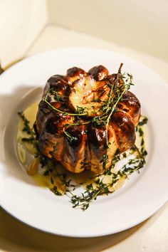 a white plate topped with meat covered in sauce and garnished with green herbs