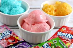 three bowls filled with different colored ice creams on top of a white wooden table