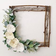 a white flower wreath hanging on the wall next to a wooden frame with branches and leaves