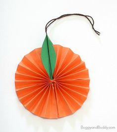 an orange origami flower hanging from a string on a white wall with a green leaf