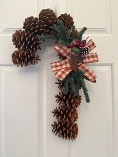 a wreath made out of pine cones hanging on the front door with red and white checkered ribbon