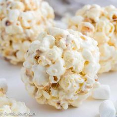 white chocolate popcorn balls with marshmallows scattered around them on a white surface