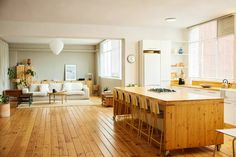 an open kitchen and living room with wood flooring, white furniture and windows in the background