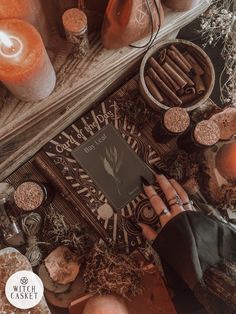 a person holding a book on top of a table with candles and other items around it