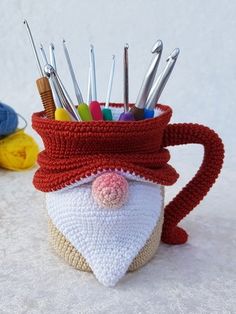 a crocheted cup with scissors and knitting needles in it on a white surface