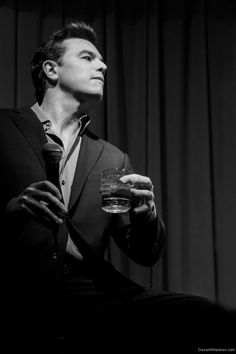 a man in a suit and tie holding a glass of water while sitting on a chair