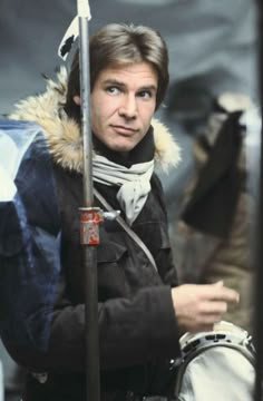 a man in winter clothes holding a pole and looking at the camera with an intense look on his face