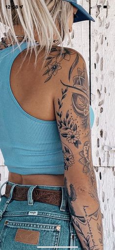 a woman with tattoos on her arms and shoulder standing in front of a white wall