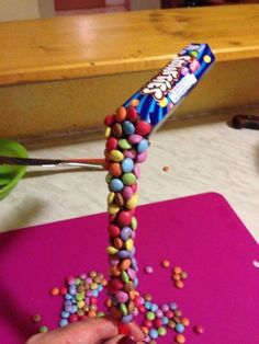 a candy bar being sprinkled with multicolored candies on a pink cutting board