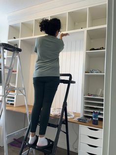 a woman standing on a ladder in front of a white bookcase and shelving