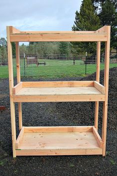 a wooden shelf sitting in the middle of a field next to a fence and grass