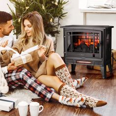 a man and woman sitting on the floor in front of an open fire place with presents