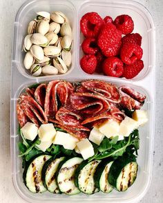 there are many different types of food in the plastic trays on this table, including cucumbers, raspberries, and almonds