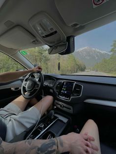 a man driving a car on a road with mountains in the background