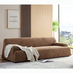 a brown couch sitting on top of a white rug in a living room next to a window