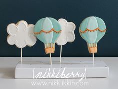 three decorated hot air balloons on top of a white cake stand with blue and gold icing