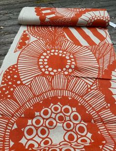 an orange and white table runner on top of a wooden floor next to a roll of fabric