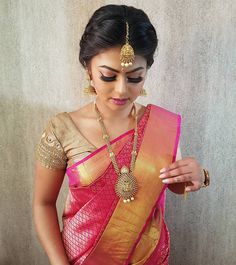 a woman in a pink and gold sari with jewelry on her neck, looking down